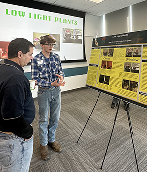 Professor Rudy Ortiz listens to an El Capitan High School student's poster presentation about plants that need low light.